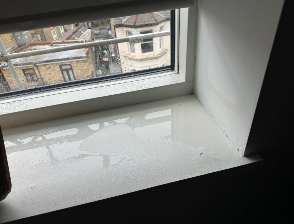 Water ingress inside a Hafer Road flat. Pooling water on the windowsill, scaffolding visible outside during roof repair.